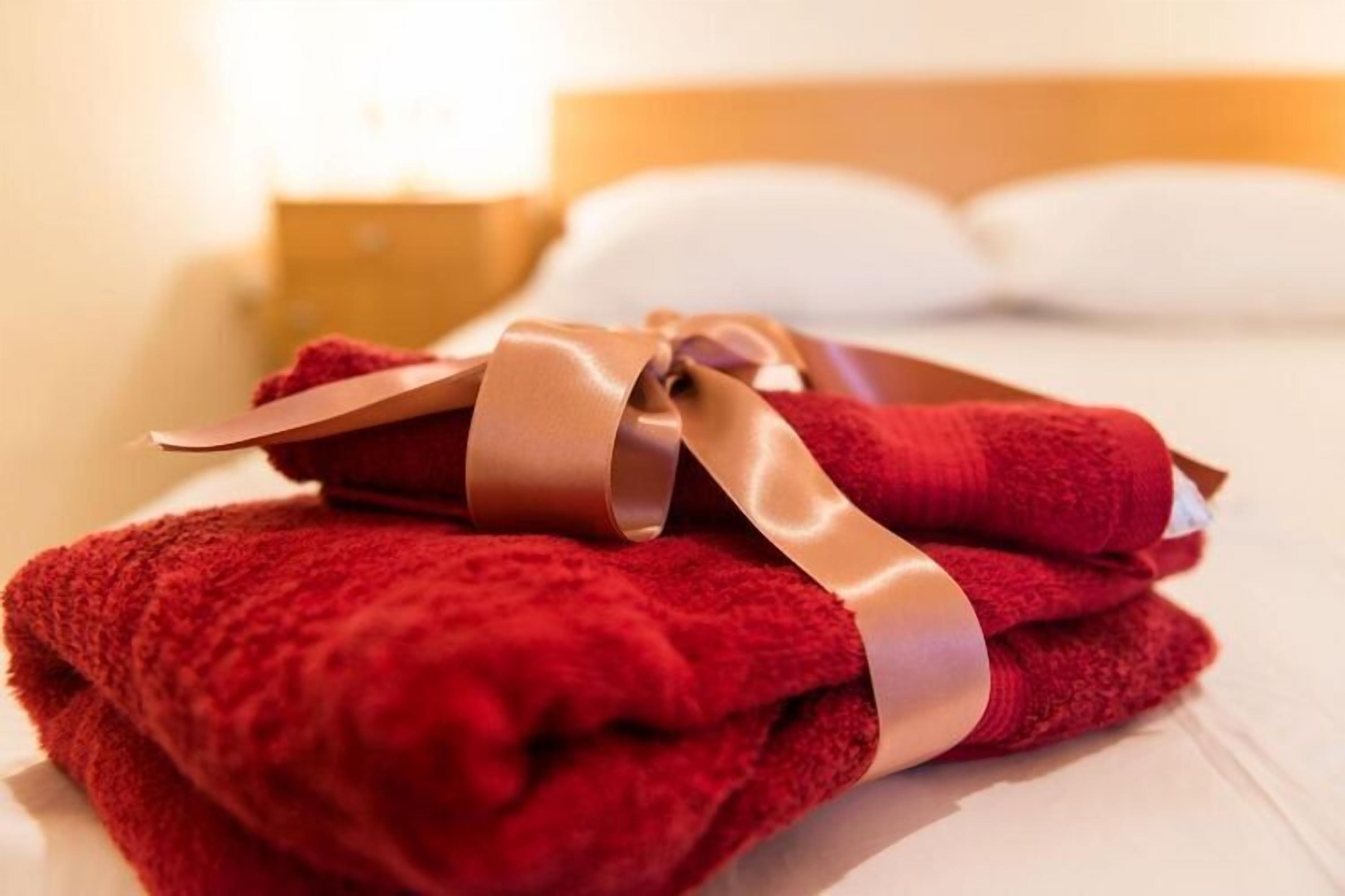 A neatly folded red towel with a satin ribbon on a bed.