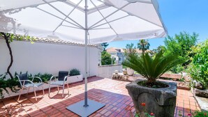 A patio area with a white umbrella, two chairs, and potted plants.