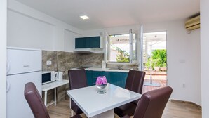 A modern kitchen with a white countertop, a microwave, and a kettle. There is a dining area with a white table and brown chairs.