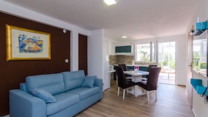 A modern living room with a blue sofa, a dining area with a table and chairs, and a kitchen in the background.