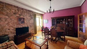 Una sala de estar con pared de piedra, televisor, mesa de centro de vidrio y comedor con sillas y un armario.