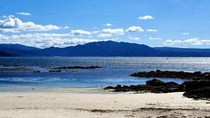 Una playa con cielos despejados, agua tranquila y montañas a lo lejos.