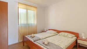 Una habitación con dos camas individuales, suelo de madera, ventana con cortinas, una mesita de noche con lámpara y un aparador.