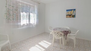 Una habitación con una mesa de comedor, sillas, una ventana con cortinas translúcidas y un cuadro en la pared.