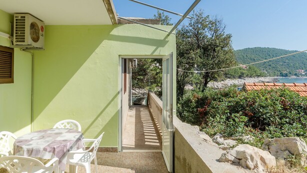Un balcón con mesa y sillas, vista al mar y una pared verde.