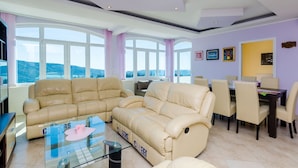 A modern living room with a beige sectional sofa, a glass coffee table, and a dining area with a dark wooden table and matching chairs.