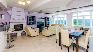 A modern living room with a fireplace, comfortable seating, a dining area, and large windows offering a scenic view.