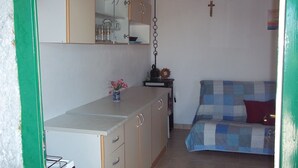 Una habitación pequeña y acogedora con kitchenette, una cama con manta a cuadros y una cruz colgada.