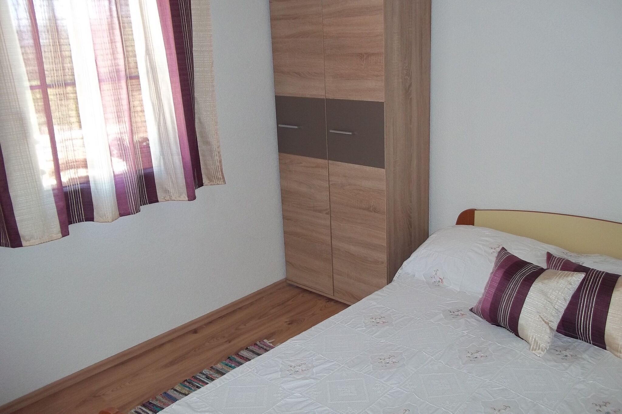 Een slaapkamer met een bed, een houten garderobe en een raam met gordijnen.
