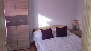 Un dormitorio con cama, dos almohadas, una mesita de noche, una lámpara y un armario.