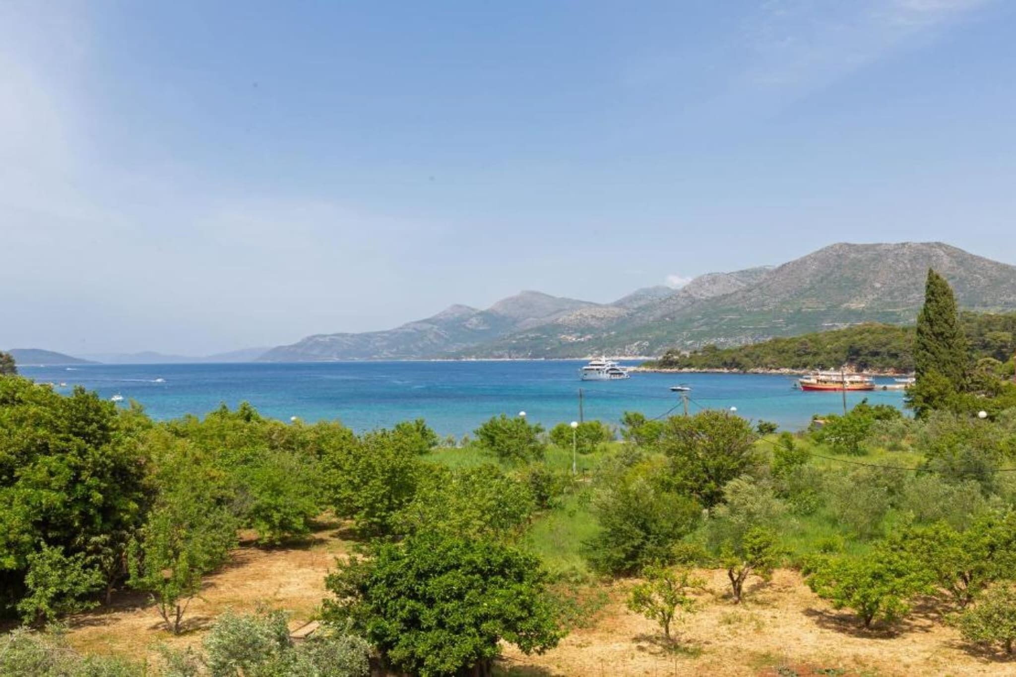 Un paysage côtier offrant une vue dégagée sur la mer, des bateaux et des montagnes en arrière-plan.