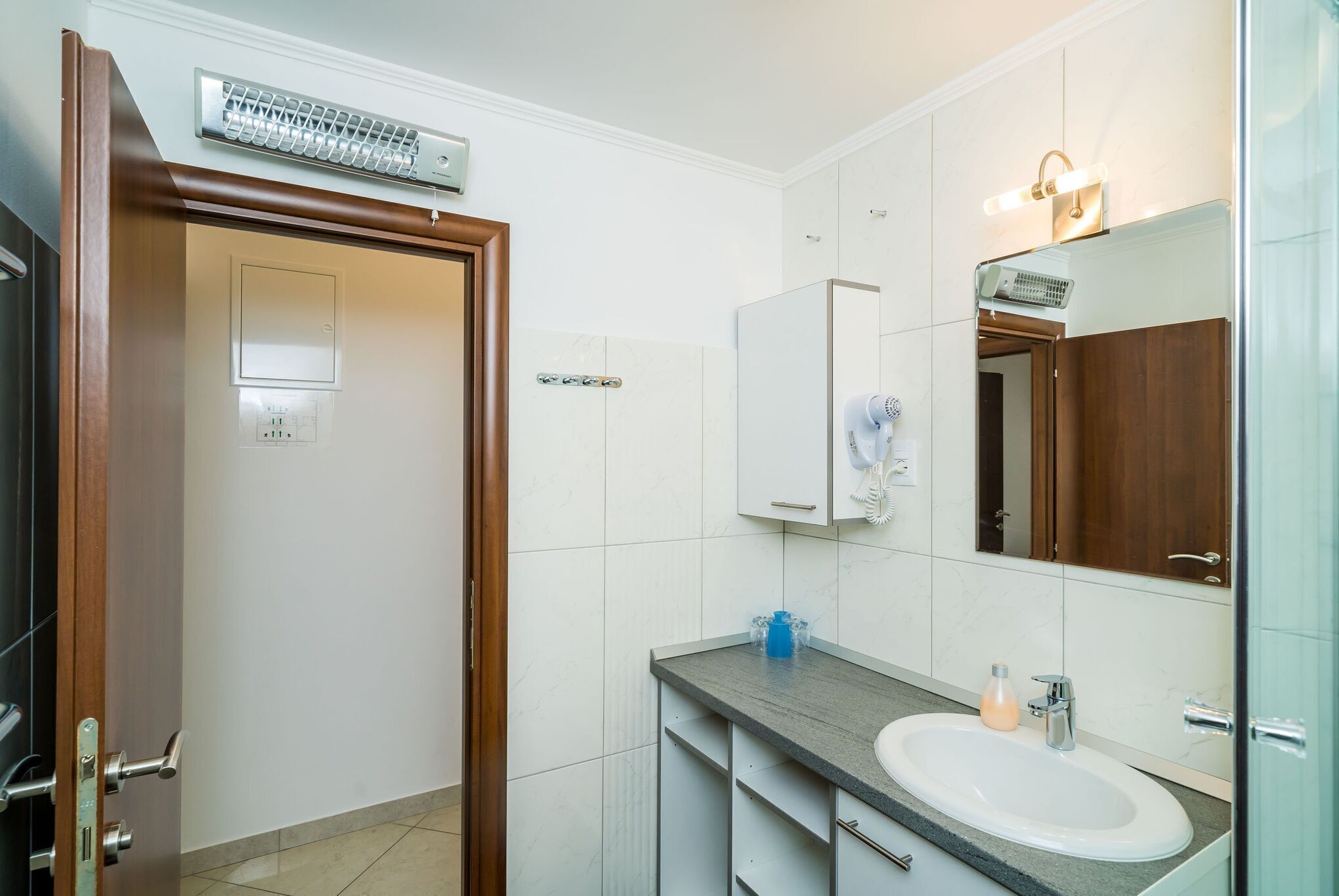 A bathroom with a wooden door, a white sink, a mirror, and a towel rack.