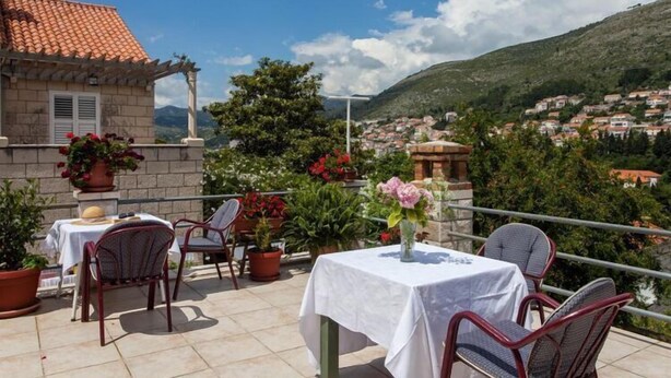 Une terrasse extérieure avec une table et des chaises, des plantes en pot et une vue sur une ville située sur une colline.