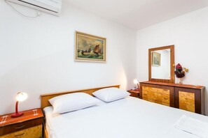 A hotel room with a bed, bedside table, lamp, dresser, mirror, and artwork on the wall. - Guest House Raguz - Double Room - 2 (Dubrovnik)