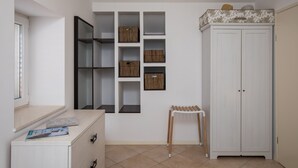 A room with a white wardrobe, a small table with a chair, and a wall-mounted shelf unit with boxes. - Apartments Odin - One-Bedroom Apartment with Terrace and Sea View - 4 (Dubrovnik)