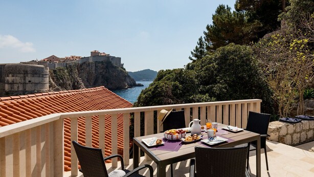 A balcony with a table set for breakfast overlooking a coastal view with a historic fort. - Apartments Odin - One-Bedroom Apartment with Terrace and Sea View - 4 (Dubrovnik)
