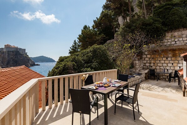 A terrace with a table set for dining, overlooking a coastal area with a historic building.