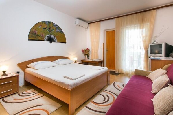 A hotel room with a large bed, a bedside table with a lamp, a TV, and a painting on the wall.