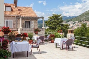 A terrace with tables and chairs, potted plants, and a view of a town.
