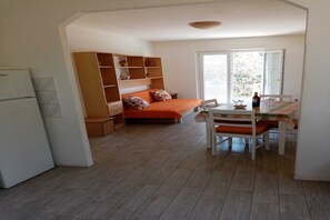 A compact room with a bed, a dining table, and a built-in shelving unit.