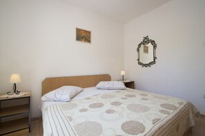 Un lit bien fait, recouvert d’une couvre-lit à motifs, avec deux lampes de chevet, une petite table de chevet et un miroir fixé au mur.