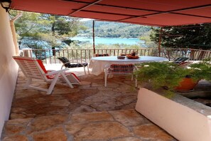 Une terrasse avec un sol en pierre, une table ronde et deux chaises dotées de coussins rouges.