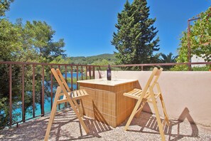 Un espace extérieur aménagé avec des meubles en bois, comprenant une table et des chaises, offrant une vue sur une étendue d’eau et des arbres.