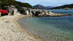 A pebble beach with clear water, rocky formations, and a distant mountain. - Guest House Simunovic - Double Room No3 (Sipanska Luka)