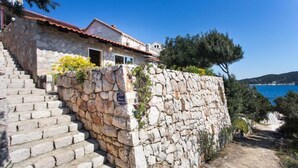 A stone staircase leading to a stone house with a red roof, surrounded by greenery and a clear blue sea in the background. - Guest House Simunovic - Double Room No3 (Sipanska Luka)