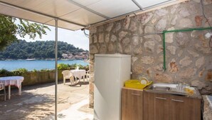 A covered outdoor area with a stone wall, a refrigerator, a sink, and a table with chairs. - Guest House Simunovic - Double Room No3 (Sipanska Luka)