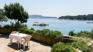 A table with chairs set on a patio overlooking a calm sea with rocky outcrops and greenery. - Guest House Simunovic - Double Room No3 (Sipanska Luka)