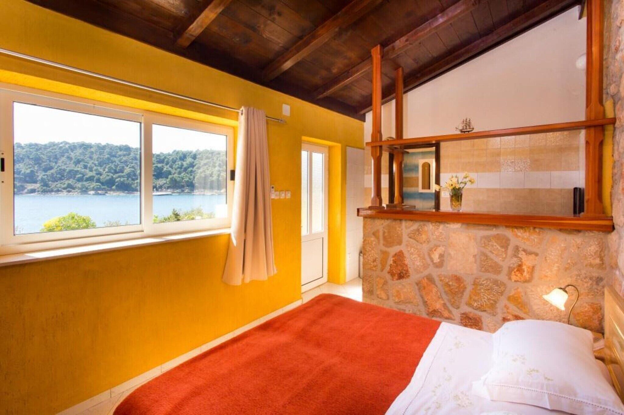 A room with a bed, a stone wall, a window with a view of a lake, and a wooden ceiling.