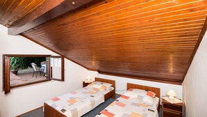 Un dormitorio con dos camas individuales, vigas de madera en el techo, un ventanal pequeño y vistas a un espacio exterior.