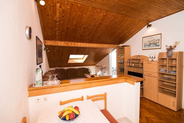 Una cocina acogedora con vigas de madera, un comedor con una mesa dispuesta para dos personas, y vista del salón contiguo.