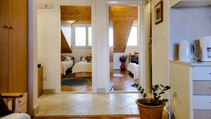 Un dormitorio con techo de madera, una cama y una mesita de noche. Se observa una ventana con persianas y un reloj en la pared.