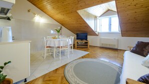 Una habitación acogedora y bien iluminada con techo de madera, una zona de comedor con mesa y sillas, un televisor y un sofá con un cojín.