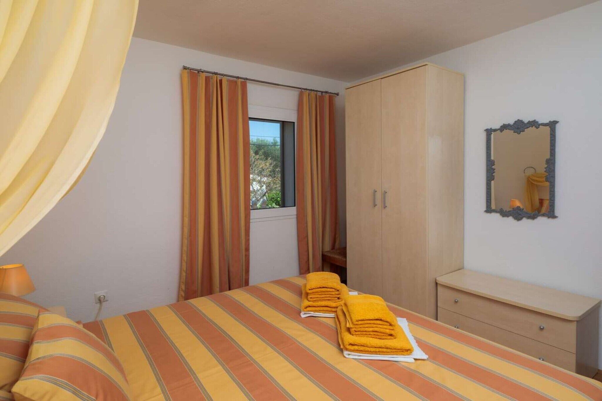 A bedroom with a bed, curtains, a wardrobe, a mirror, and a window.