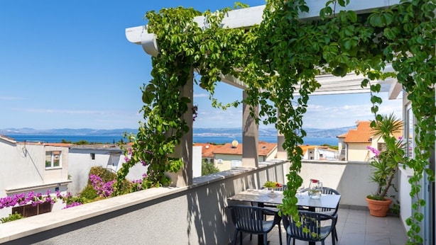 A balcony with a table and chairs, a pergola with greenery, and a view of the sea and buildings. - Apartment Oaza - Three Bedroom Apartment with Terrace and Sea View (Supetar)
