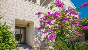 A modern building with a white facade, a balcony, and vibrant pink bougainvillea flowers. - Apartment Oaza - Three Bedroom Apartment with Terrace and Sea View (Supetar)