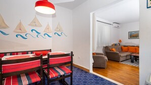 A dining area with a table and chairs, a living room with a sofa and a painting, and a hallway with a blue patterned floor. - Apartment Oaza - Three Bedroom Apartment with Terrace and Sea View (Supetar)