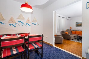 A dining area with a table and chairs, a living room with a sofa and a painting, and a hallway with a blue patterned floor. - Apartment Oaza - Three Bedroom Apartment with Terrace and Sea View (Supetar)