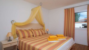 A bed with striped bedding, a bedside table with a lamp, and a window with curtains. - Apartment Oaza - Three Bedroom Apartment with Terrace and Sea View (Supetar)