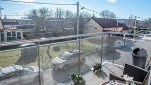 Ein Balkon mit Blick auf geparkte Autos und Häuser, einem Metallgeländer und Gartenmöbeln.