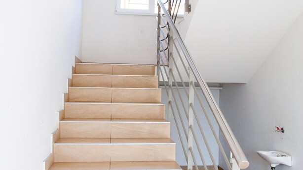 Eine Holztreppe mit Metallgeländer, einer weißen Wand und einem Fenster.