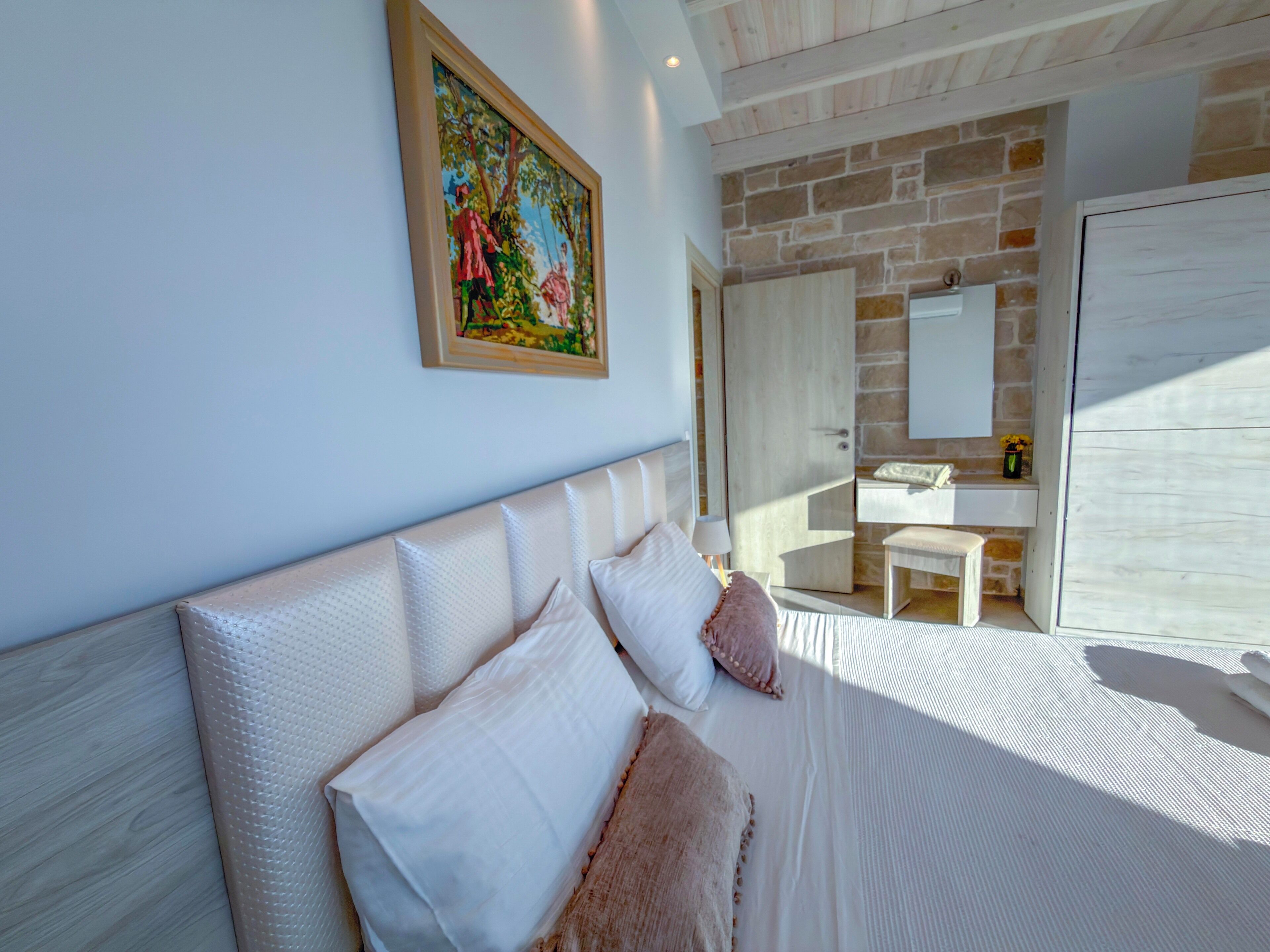 A bedroom with a large bed, a painting on the wall, a stone wall, and a wooden door.
