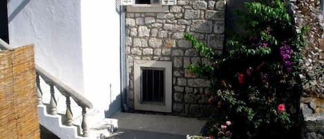 A narrow stone pathway leading to a white building with a small door and a window with shutters.
