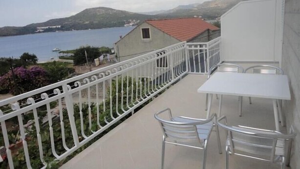 A balcony with a white railing, a table, and two chairs.