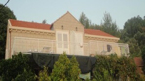 A two-story building with a red-tiled roof, white shutters, and a balcony with a metal railing.