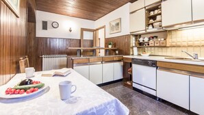 Una cocina con armarios de madera, un lavamanos y una encimera. Hay un reloj en la pared y una ventana con contraventanas de madera.