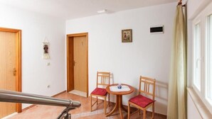 Une pièce avec une porte en bois, une petite table et deux chaises, un tableau au mur et une fenêtre avec des rideaux.